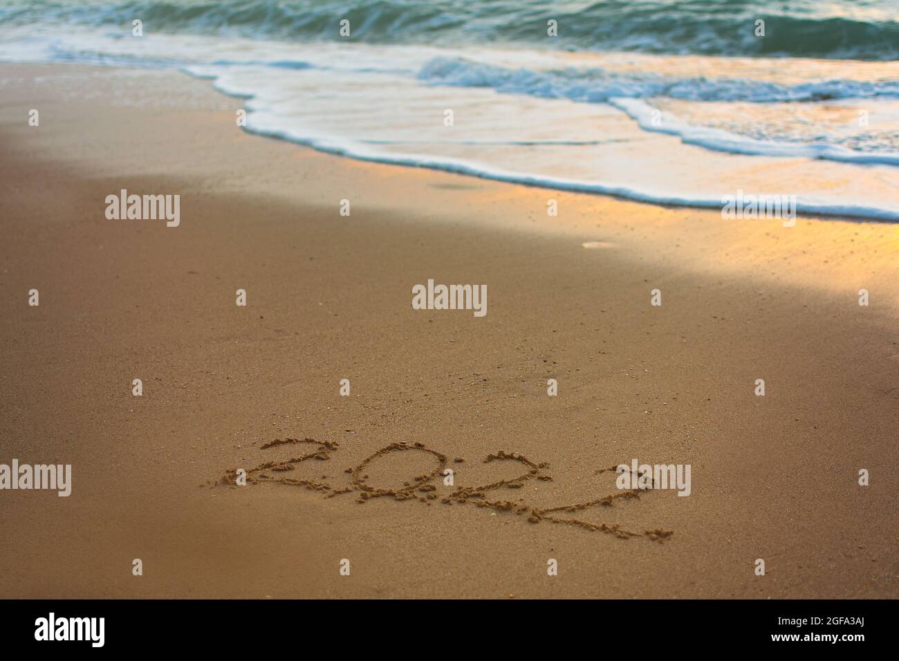 2022 bonne inscription du nouvel an plage de sable. Le texte écrit est écrit sur du sable jaune et est lavé par une vague. Le concept de changer l'année, Banque D'Images