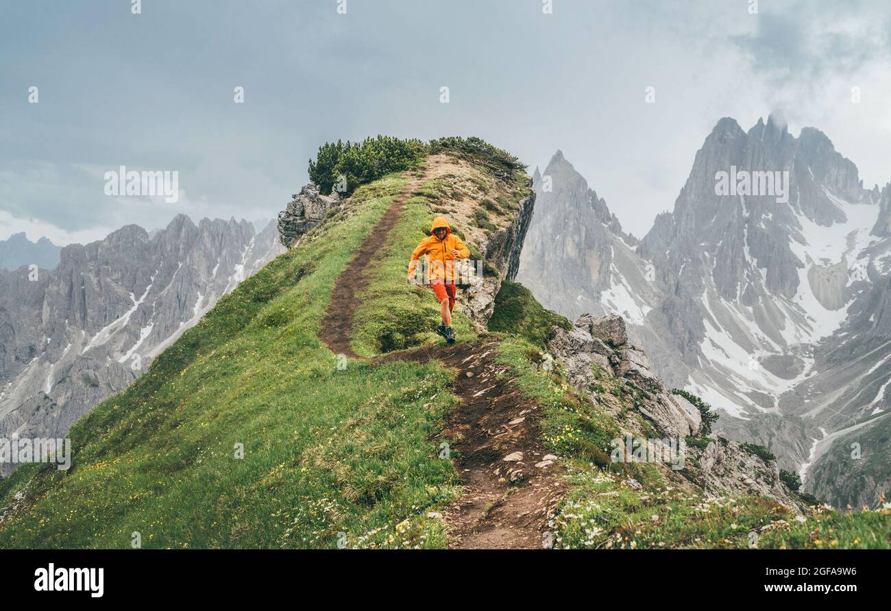 Veste de jogging en softshell orange habillée sur un sentier de montagne vert avec arrière-plan pittoresque de la chaîne des Alpes Dolomites. Actifs et Europ Banque D'Images