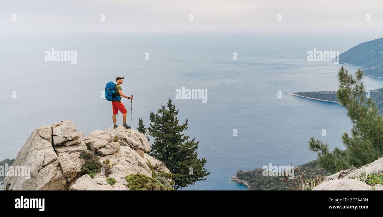 Jeune randonneur utilisant des bâtons de randonnée appréciant la mer Méditerranée sur le sommet d'une falaise pendant la randonnée de chemin lycien. Célèbre Likya Yolu turc Banque D'Images