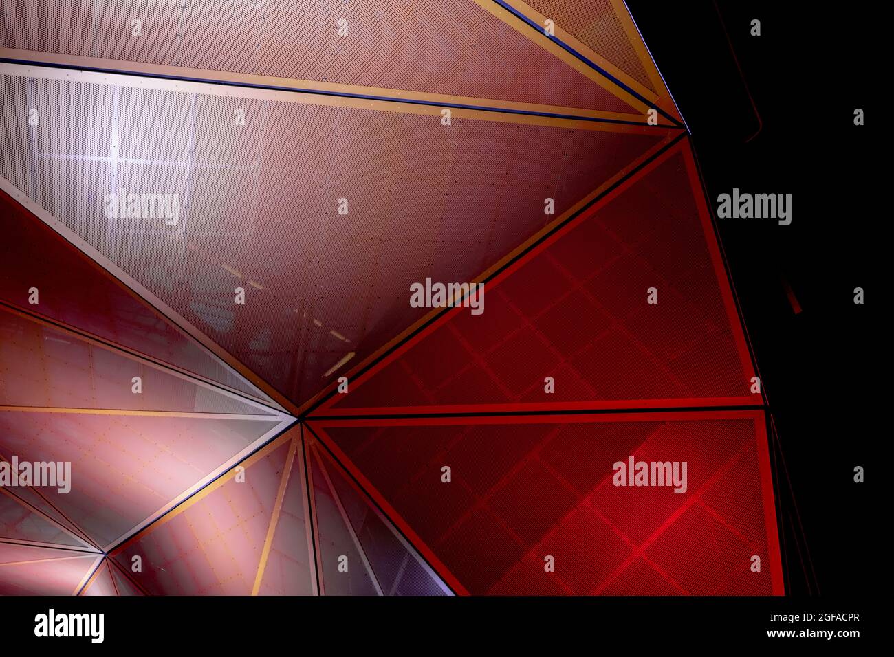 Architecture moderne. Construction métallique géométrique orange et rouge à partir de pièces triangulaires. Arrière-plan abstrait dans l'obscurité. Banque D'Images