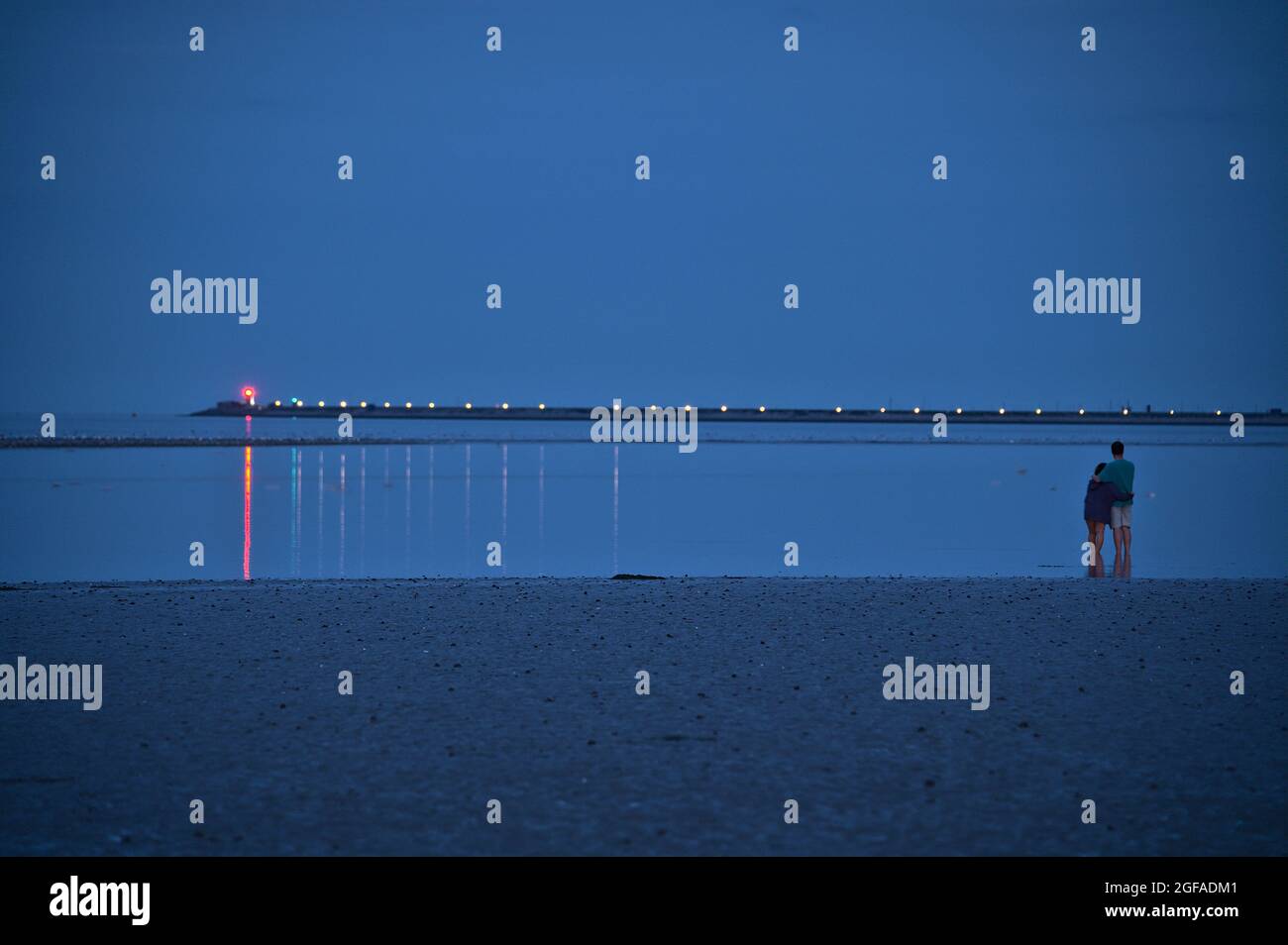 Belle vue en soirée couple debout dans l'eau et attendant l'esturgeon bleu Lune qui s'élève au-dessus du ciel irlandais Port de Dun Laoghaire le 23 août 2021 Banque D'Images