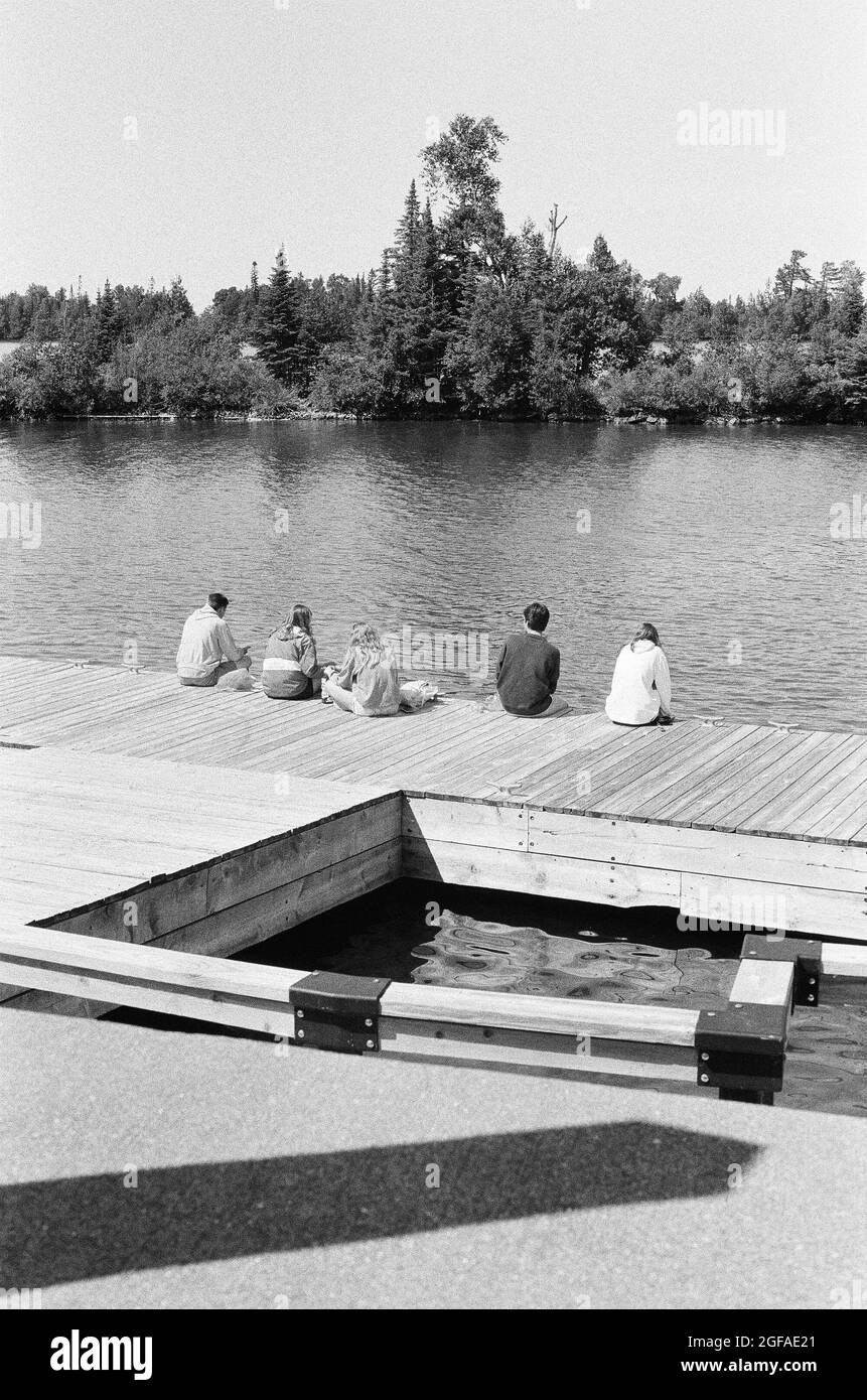 Photo arrière en niveaux de gris de personnes assises sur une promenade au bord de la rivière Banque D'Images