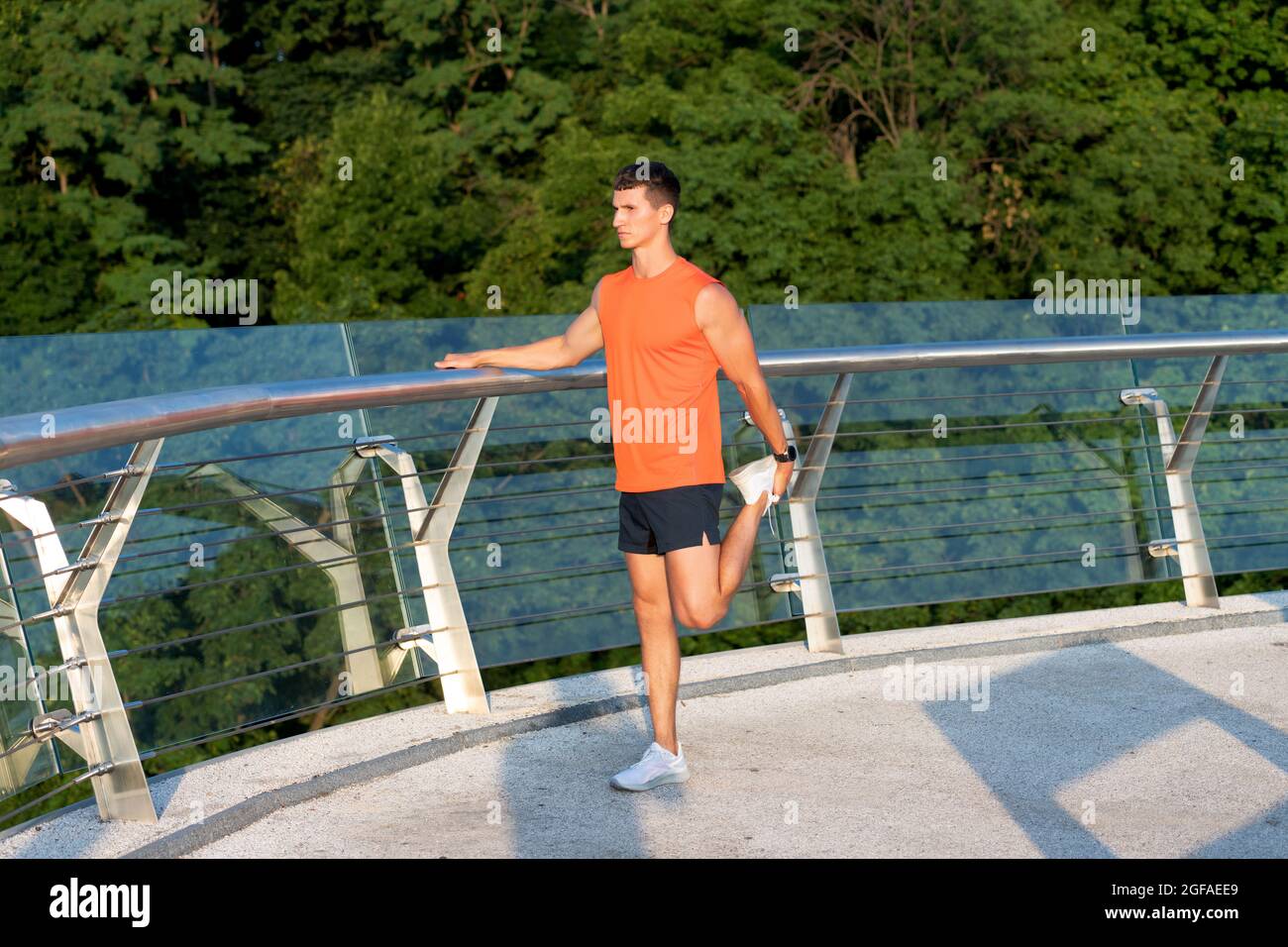 Homme sportif en vêtements de sport saisissez la cheville avec la main étirant la jambe après l'entraînement en plein air, étirez Banque D'Images