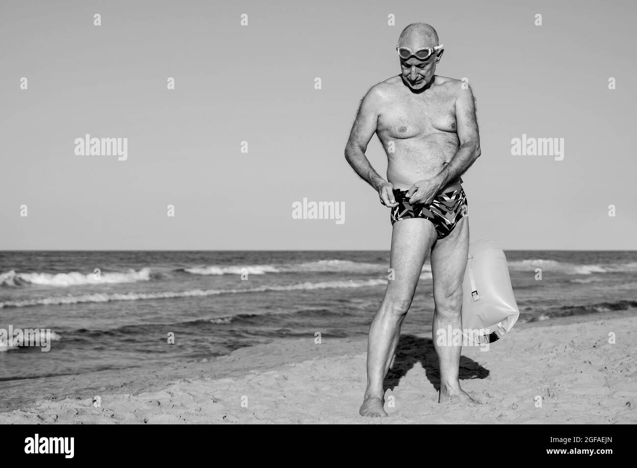 Nageur de sport homme senior entraînement pour nager en eau libre triathlon avec la plage sur fond - personnes âgées et un mode de vie sain - noir et blanc montage Banque D'Images