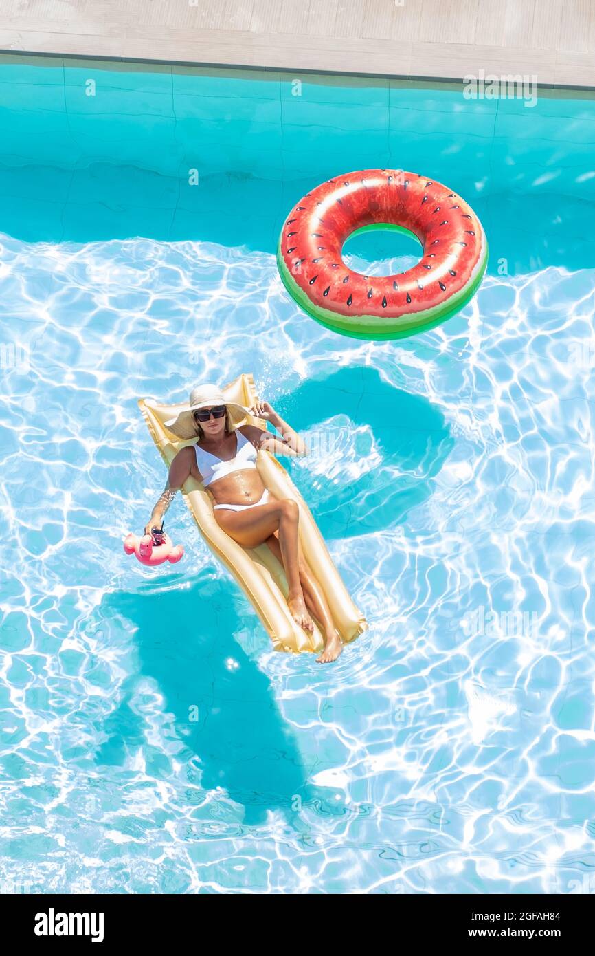 Vue de dessus d'une fille dans un maillot de bain et chapeau flottant sur matelas gonflable or dans la piscine avec un cocktail de boisson. Concept vacances d'été et détente Banque D'Images