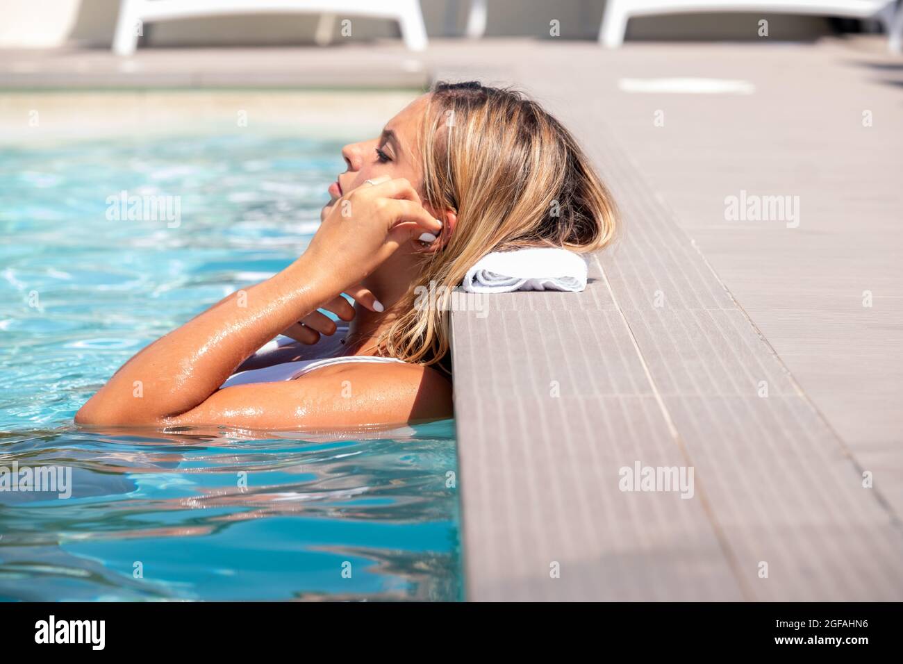 Femme détendue à l'écoute de la musique avec des écouteurs baignant dans une piscine - Portrait bonne fille se relaxant dans la piscine à l'écoute avec des écouteurs Banque D'Images