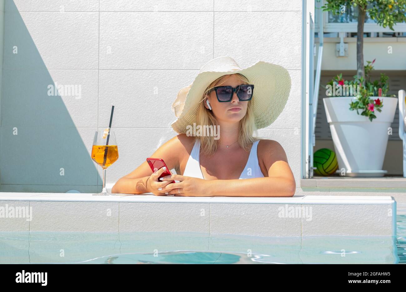 Une adolescente filant avec un smartphone rouge tout en se baignant dans une piscine en vacances d'été - une femme au téléphone envoie des SMS tout en se relaxant Banque D'Images