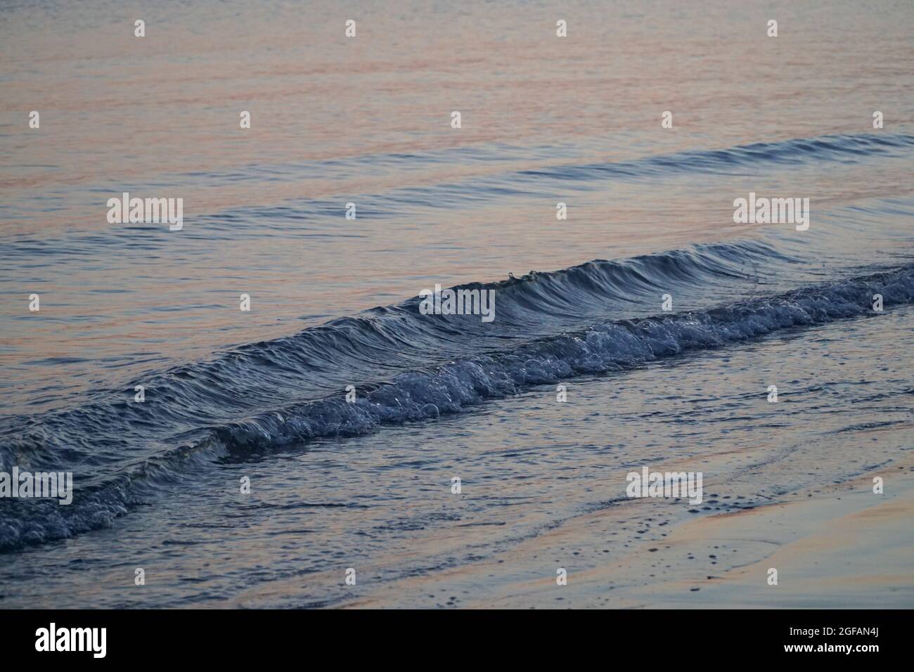 East Wittering, Royaume-Uni, 23 août 2021 : les vagues douces sur la plage de sable au crépuscule reflètent les bleus et les roses dans le ciel juste après le coucher du soleil. La mer est l'Engli Banque D'Images