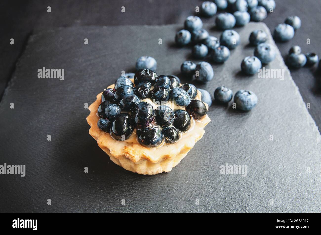 Tartes délicieuses et sucrées à base de crème et de myrtille. Tarte aux myrtilles sur fond sombre. Gâteau aux myrtilles sur une table de service noire parsemée Banque D'Images