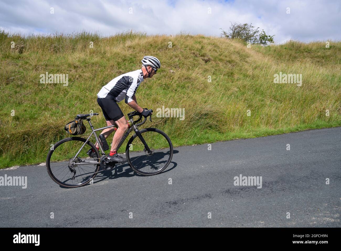 Cycliste mâle mature qui monte sur une colline, au creux de Bowland, Lancashire, Royaume-Uni. Banque D'Images