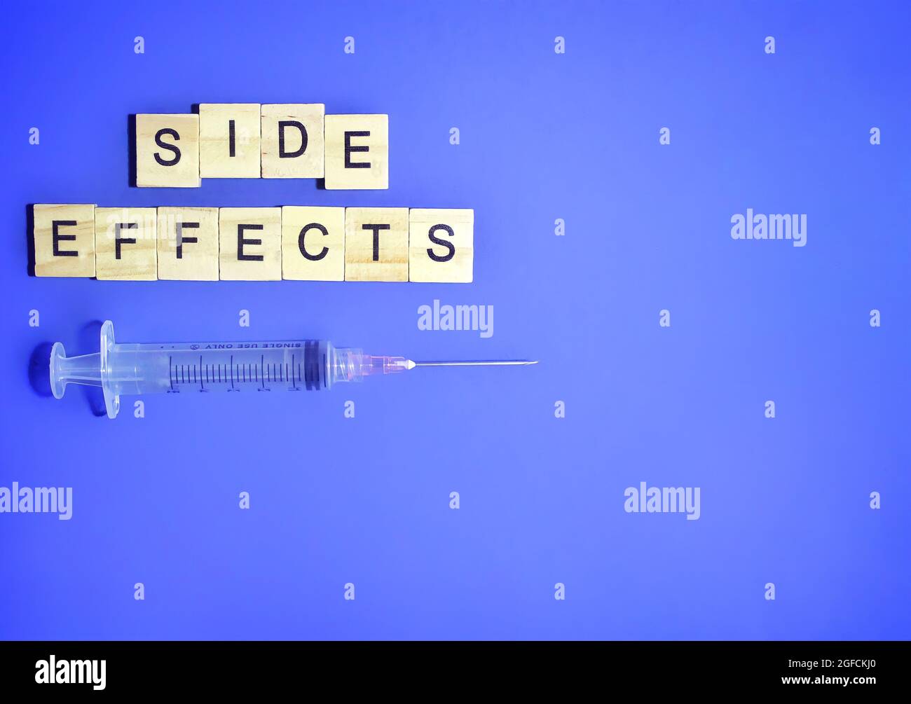 Vue de dessus de la seringue médicale et du cube en bois avec effets SECONDAIRES sur fond bleu. Copier l'espace pour le texte Banque D'Images