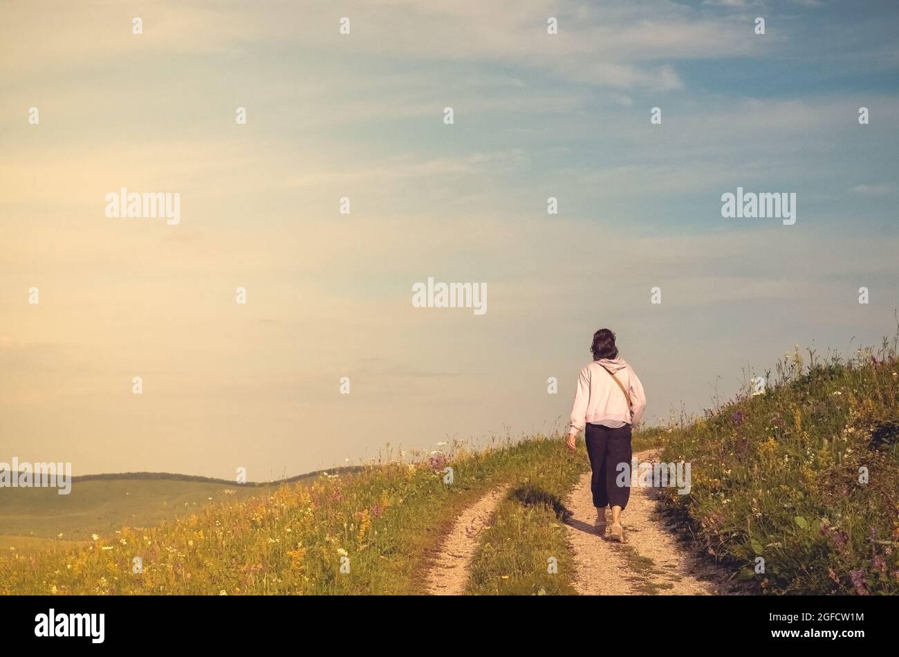 Une fille marche le long d'une route de campagne le long d'une chaîne de montagnes contre le ciel bleu. Le concept de randonnée dans la nature. Banque D'Images