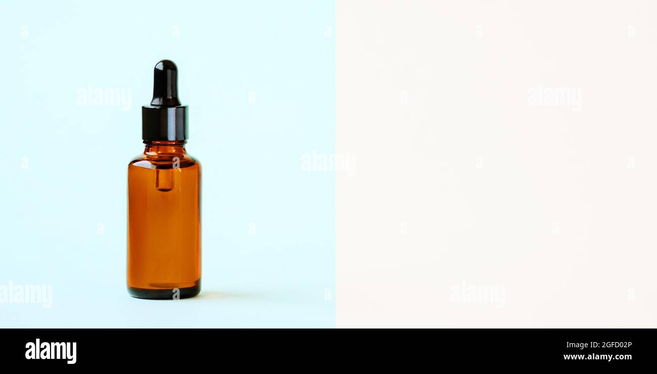 Une maquette d'un flacon compte-gouttes en verre vide en verre ambré brun sur fond bleu. Sérum, bannière ou gabarit de soin pour la peau. Le concept d'un produit cosmétique naturel.CopySpace. Banque D'Images
