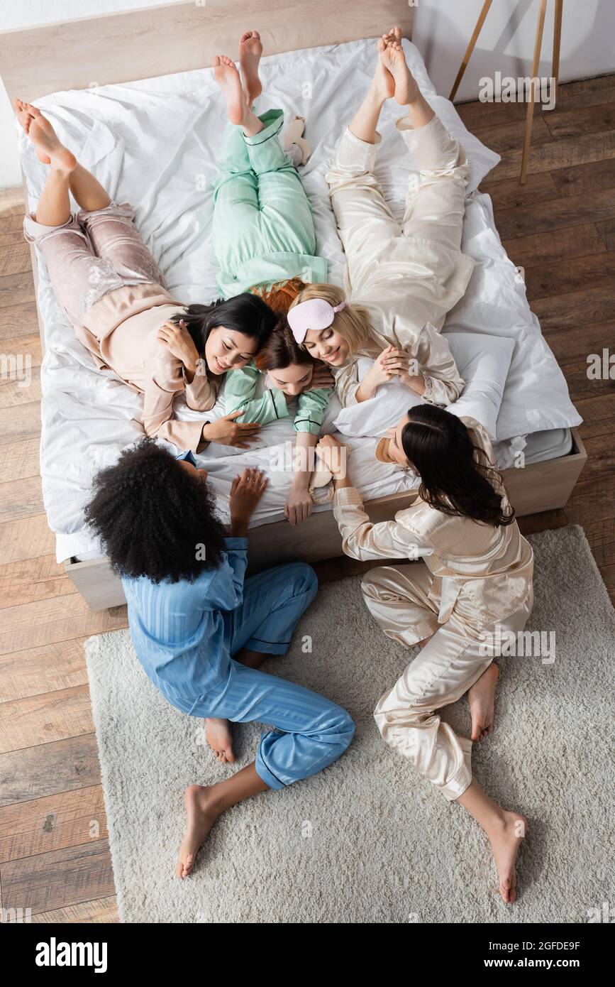 vue en grand angle des femmes interraciales souriantes qui s'allonger sur le lit pendant la fête du sommeil Banque D'Images