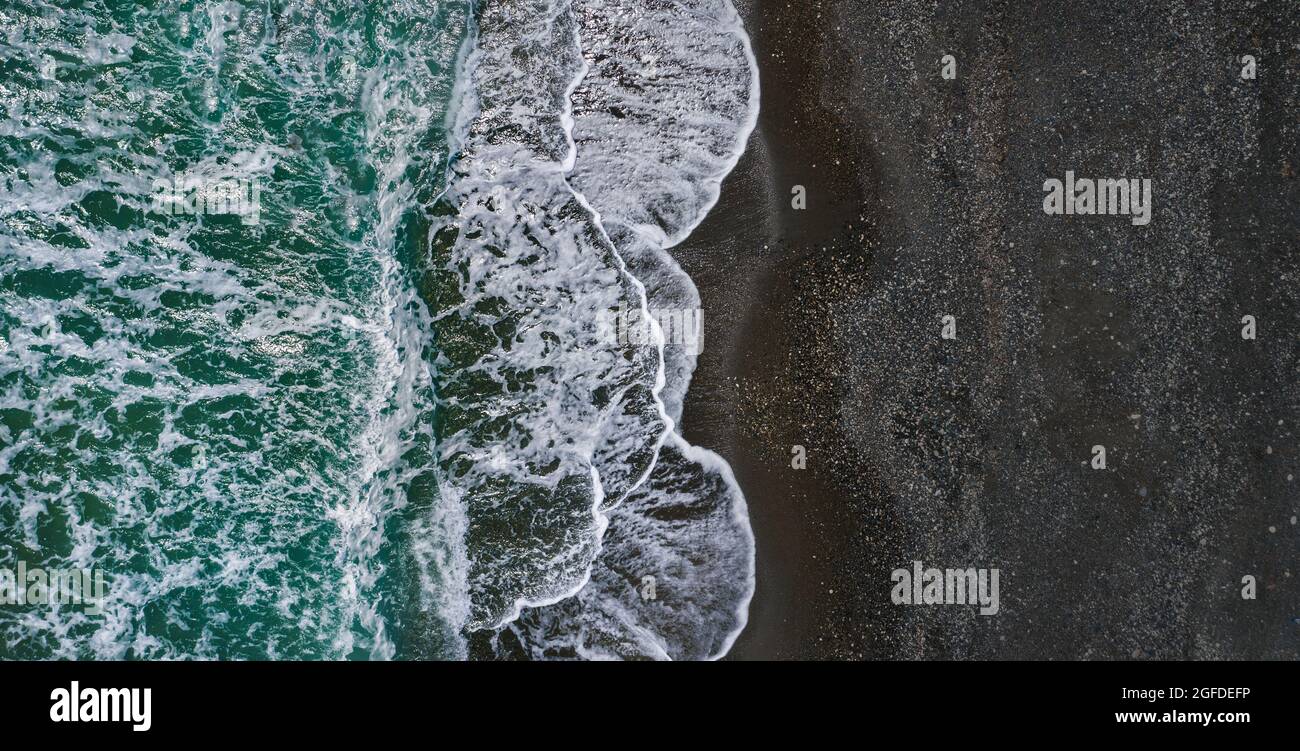 Rive de la mer avec texture spectaculaire des vagues de rupture et du sable noir, perspective de drone Banque D'Images