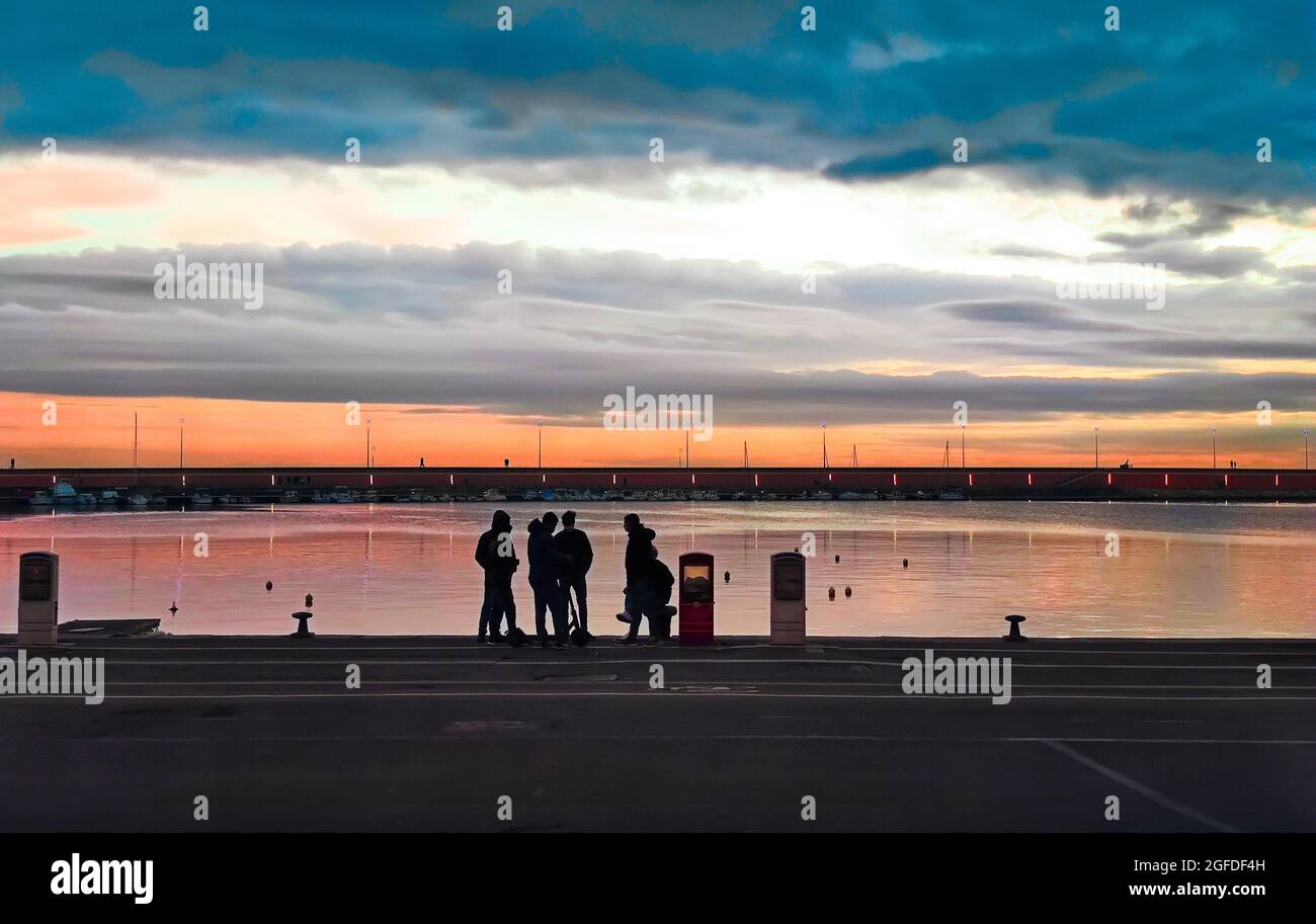 Port commercial d'Imperia Oneglia avec des groupes de personnes illuminés par la lumière du coucher du soleil, reportage de voyage Banque D'Images