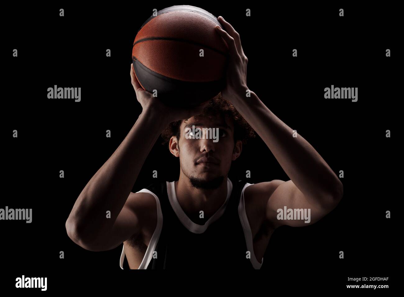 Joueur de basket-ball professionnel tenant une balle sur fond noir. Sérieux homme afro-américain concentré en uniforme sportif. Banque D'Images