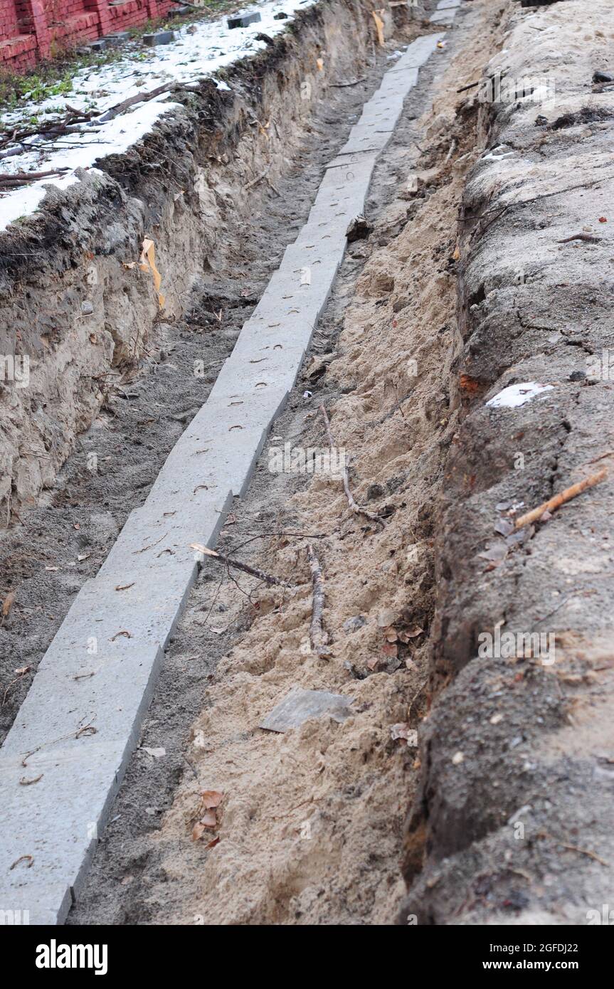 Un gros plan d'une excavation de tranchée de câble avec des câbles souterrains installés et recouverts de dalles de béton de protection pour fournir l'électricité et teleco Banque D'Images