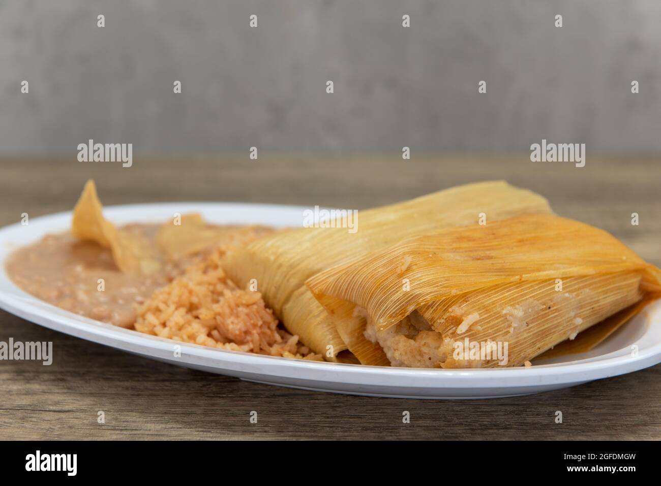 Assiette généreuse de tamales enveloppée dans une huche de maïs, servie avec du riz et des haricots réfrits. Banque D'Images