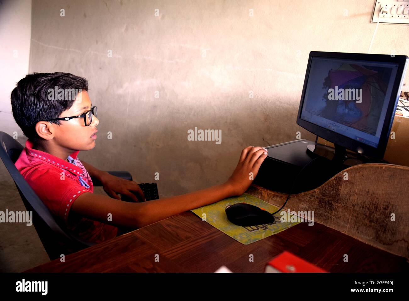 Garçon utilisant un ordinateur à l'aide de la souris et du clavier, il regarde l'image dans le système informatique. Banque D'Images