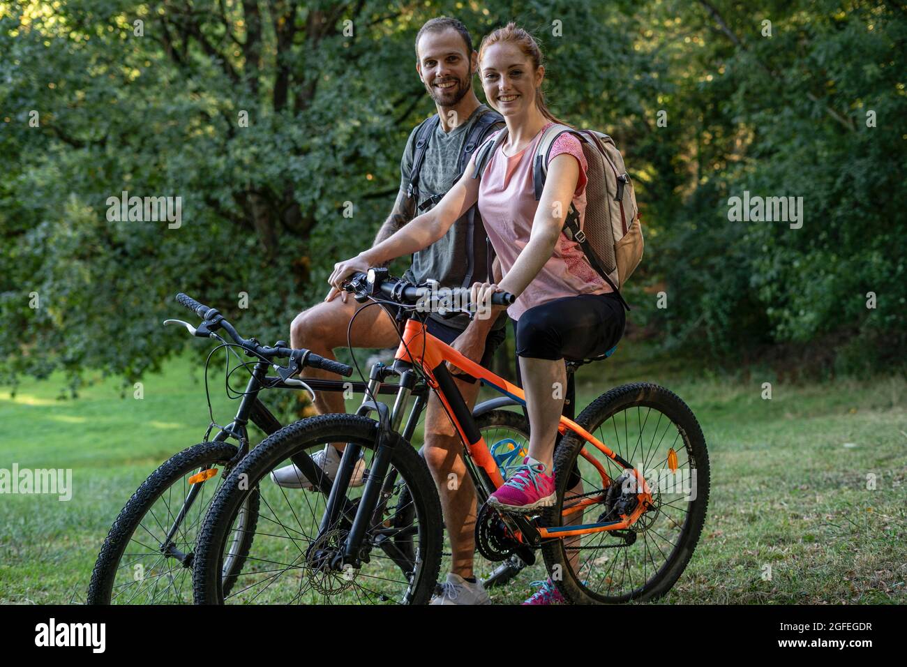 Portrait d'un jeune couple souriant assis sur des vélos en forêt Banque D'Images