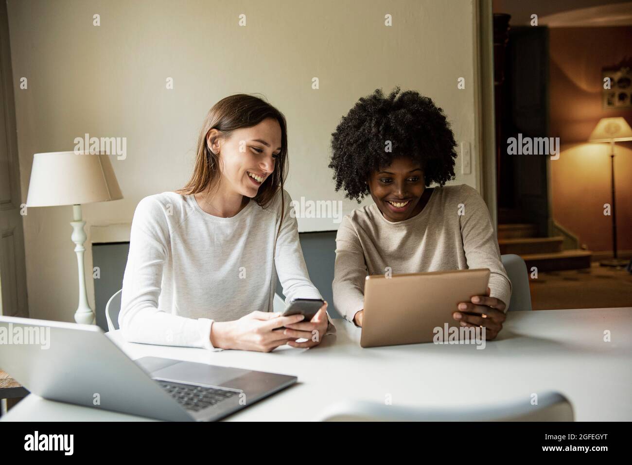 Jeunes femmes souriantes utilisant une tablette numérique et un smartphone à la maison Banque D'Images