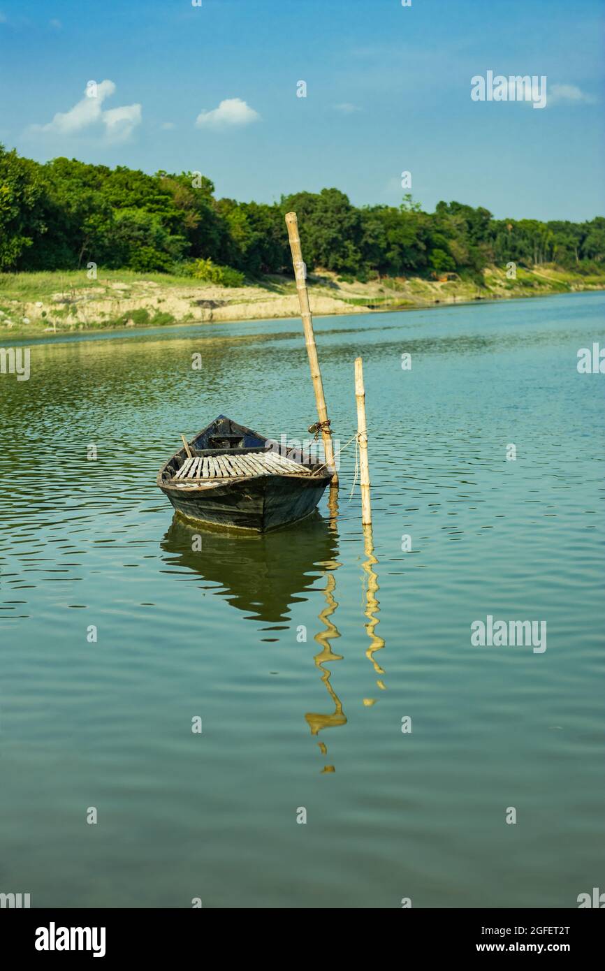 Il y a un canot relié à l'eau dans la rivière et il y a des arbres verts sur la rive et des nuages blancs dans le ciel bleu Banque D'Images