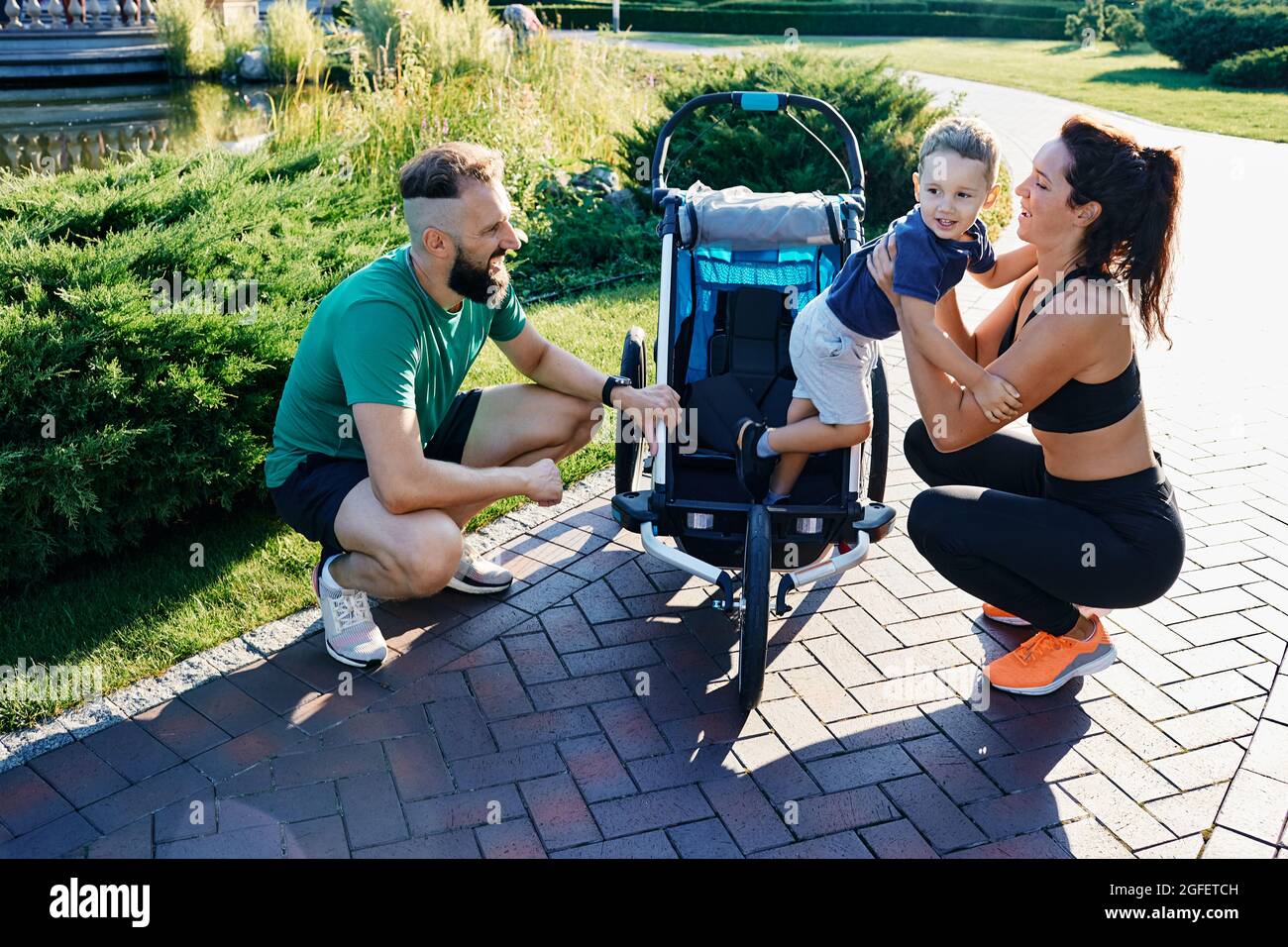 Bonne famille sportive avec un enfant près de la poussette de jogging après l'entraînement dans le parc de la ville Banque D'Images