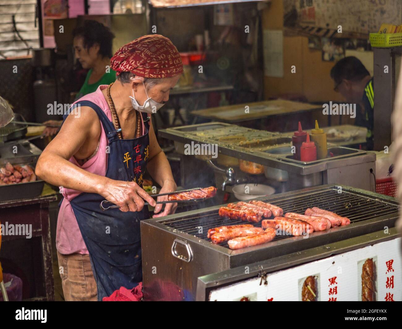 Pingxi, Taïwan - octobre 2016 : une femme taïwanaise grille une saucisse dans un bazar local typique à Taïwan, en Asie. Banque D'Images