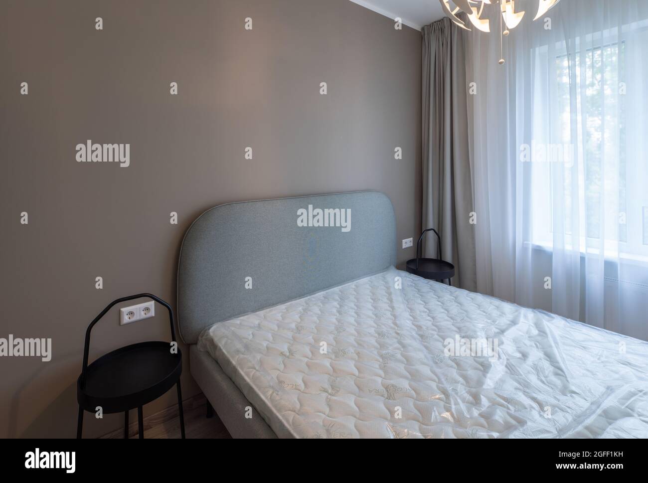 Intérieur contemporain d'une chambre rénovée dans l'appartement. Mur beige. Lit avec nouveau matelas. Tables de nuit noires. Banque D'Images