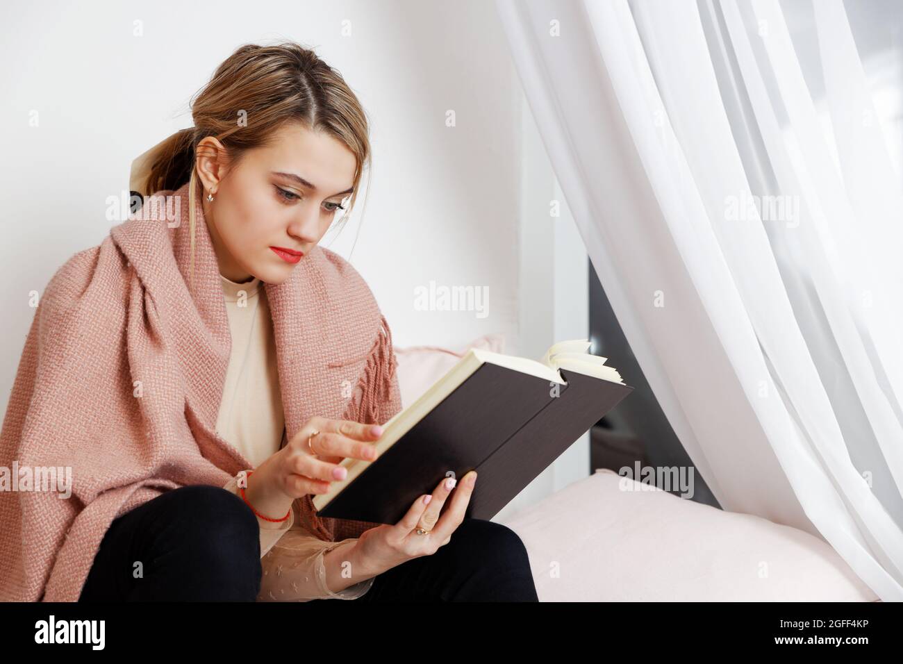 Jeune femme lisant un livre à la fenêtre le soir Banque D'Images