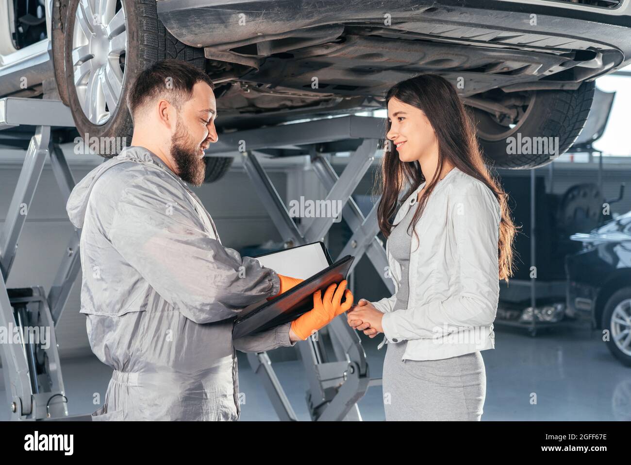 Presse-papiers de maintien Auto Mechanic discutant avec une cliente en atelier au centre de réparation automobile. Qualité de service Banque D'Images