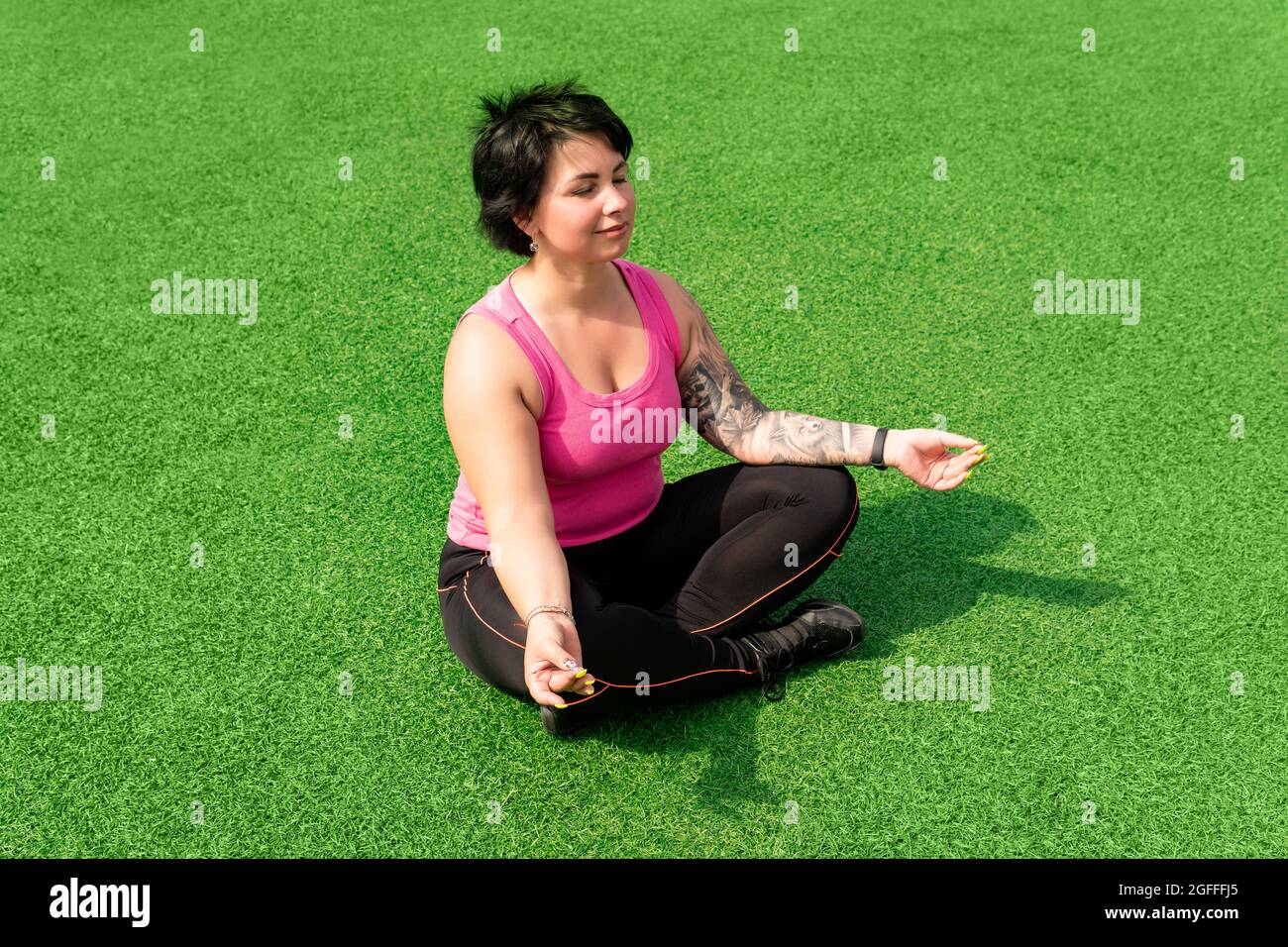 une jeune femme robuste médite sur la pelouse verte après avoir fait de l'exercice Banque D'Images