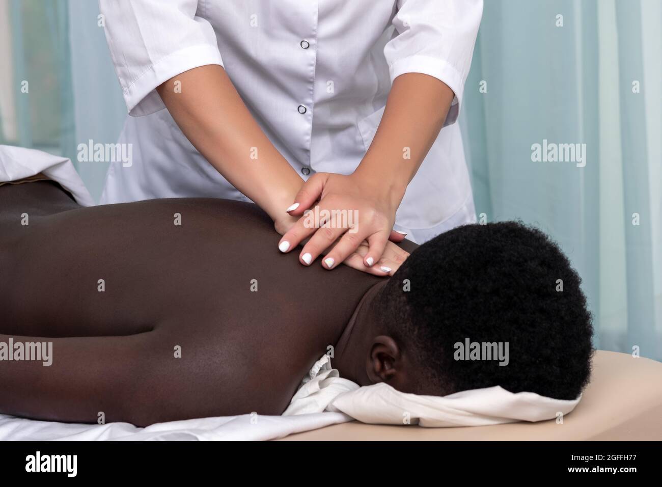 femme masseuse faisant le massage de la zone de l'épaule à l'homme noir Banque D'Images