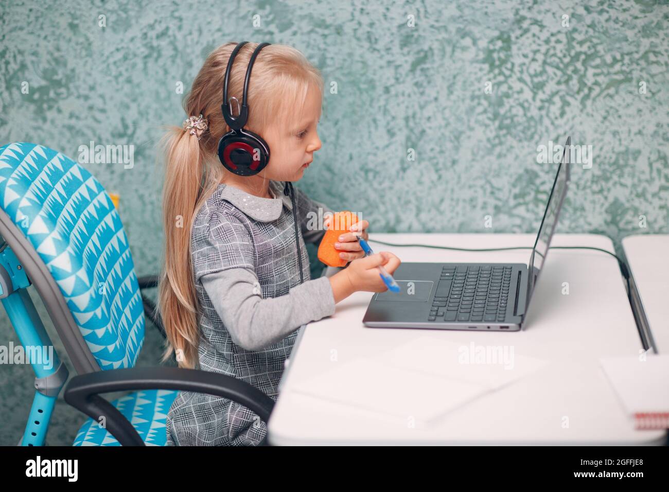 Jeune élève petite fille avec la carotte en main et ordinateur portable apprendre et se préparer à l'école. Banque D'Images