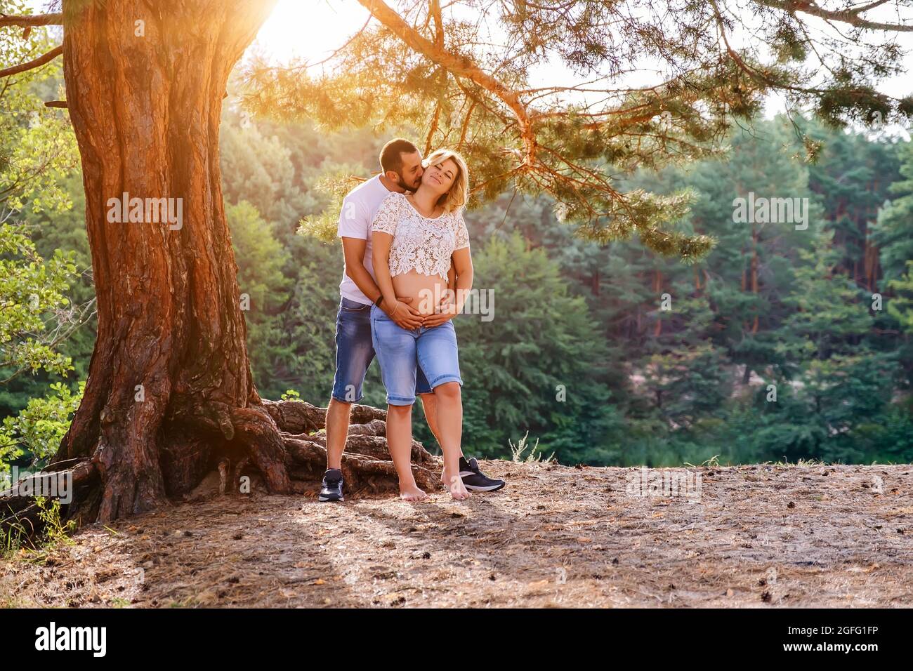 Jeune s'attendant à un couple tenant les mains sur le ventre sous l'arbre au coucher du soleil Banque D'Images