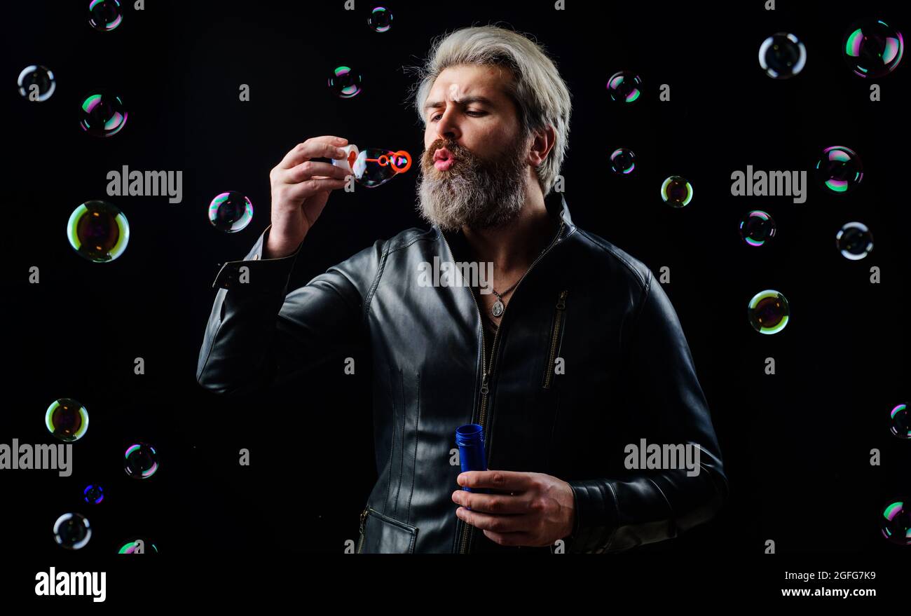 Homme barbu dans une veste en cuir soufflant de bulles de savon. Bonheur. Bonne humeur. Jouer avec des bulles. Banque D'Images