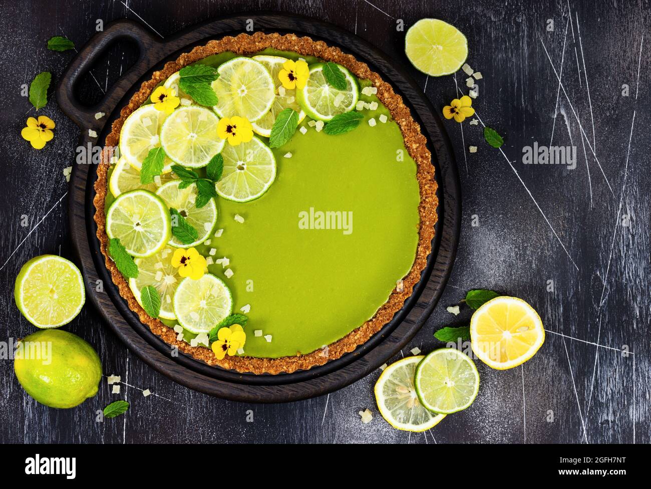Cheesecake avec des tranches de citron vert, menthe fraîche, fruits confits et fleurs de pansy sur fond de pierre sombre. Vue de dessus. Banque D'Images
