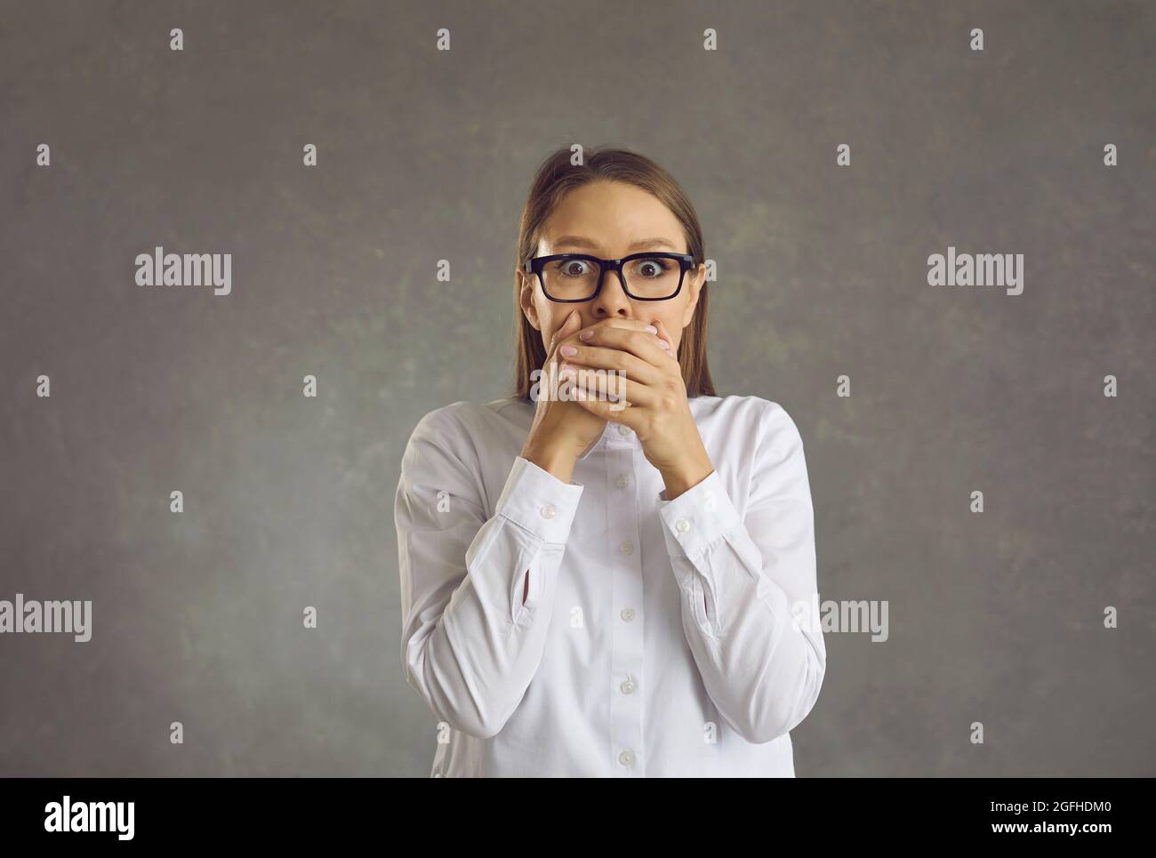 Jeune femme choquée dans les lunettes avec la main au-dessus de la bouche portrait de studio tourné Banque D'Images