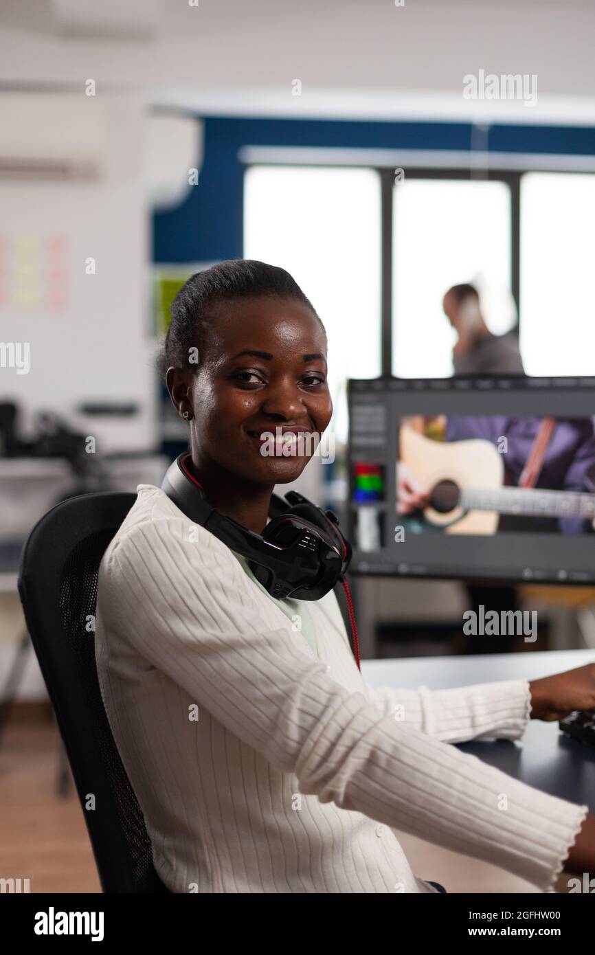 Éditeur de vidéo afro-américain artiste regardant la caméra souriant montage vidéo projet créatif dans le logiciel de post-production travaillant dans startup studio bureau. Montage de films audio par un vidéaste Banque D'Images