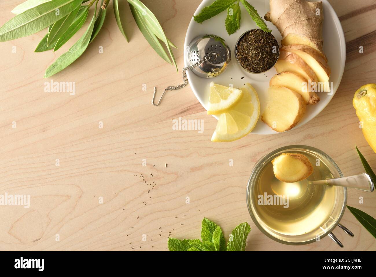 Tasse de thé vert avec citron au gingembre et menthe sur table en bois avec racine en tranches et passoire en métal remplie de thé sur plat blanc et feuilles sur patte en bois Banque D'Images