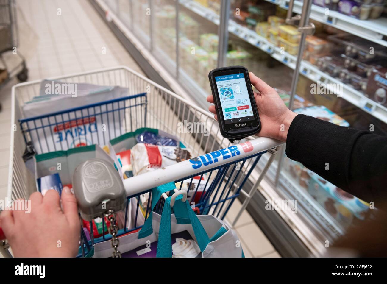 Supermarché Super U: Femme, préparateur de commande / emballeur sélection de produits dans une section du supermarché à l'aide d'un appareil mobile pour vérifier l'ordre du client Banque D'Images