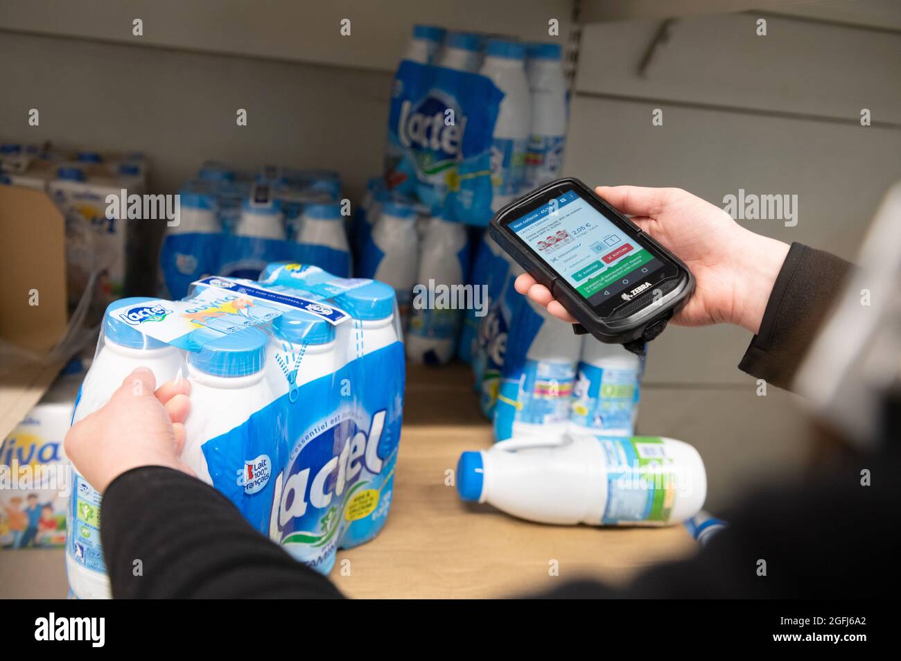Supermarché Super U: Femme, préparateur de commande / emballeur sélection de produits dans une section du supermarché à l'aide d'un appareil mobile pour vérifier l'ordre du client Banque D'Images