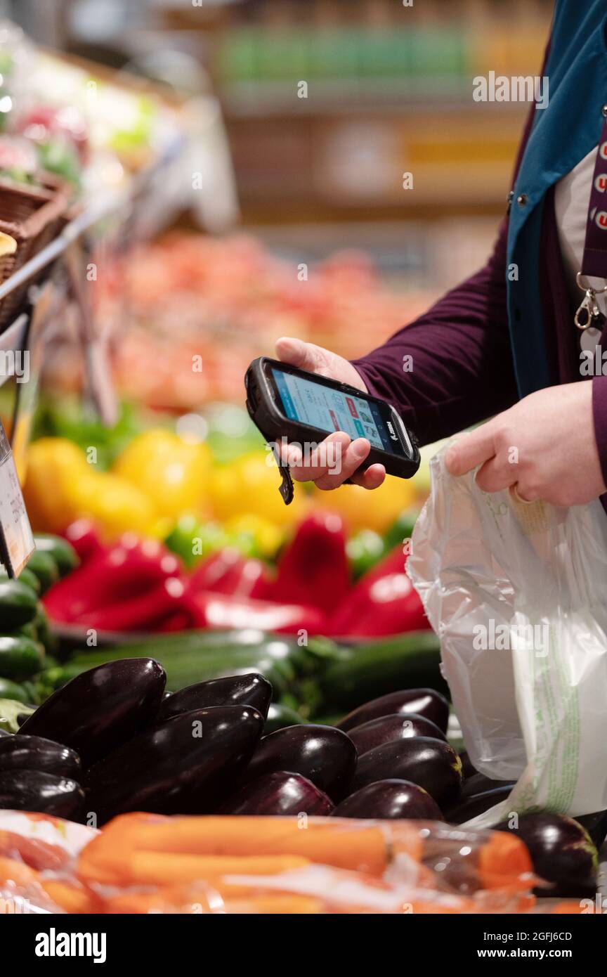 Super U supermarché: Femme, préparateur de commande / emballeur sélection de produits dans le département des fruits et légumes d'un supermarché en utilisant un appareil mobile à c Banque D'Images