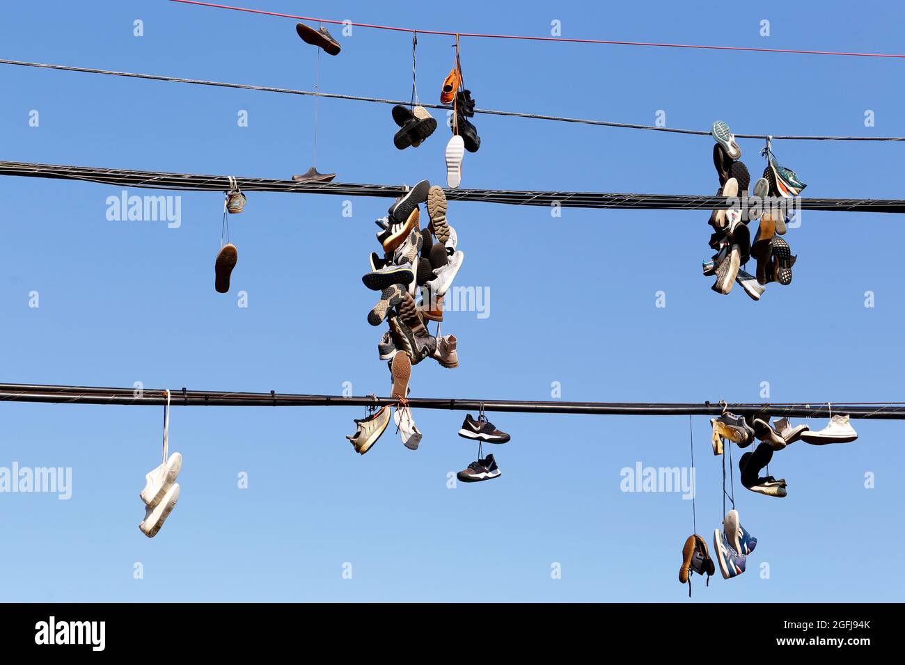chaussures, baskets accrochées à un fil téléphonique contre un ciel bleu ensoleillé ; baskets attachées ensemble et jetées sur une ligne électrique. Banque D'Images
