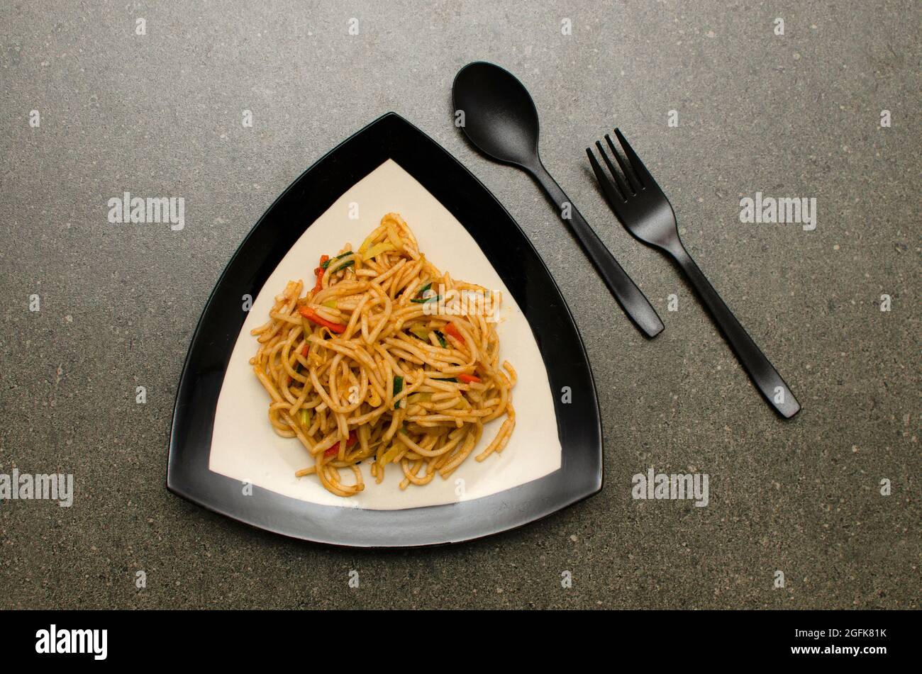 Légumes Schezwan Hakka nouilles servies dans une plaque de verre sur fond gris Banque D'Images