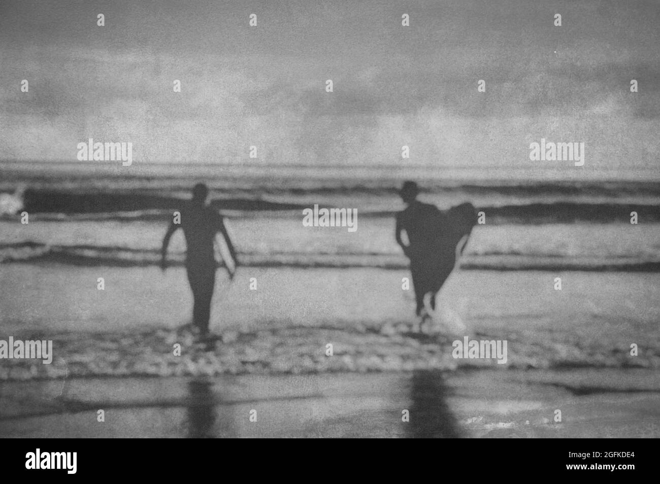 Silhouette de surfeurs transportant leur planche de surf dans la mer, effet filtre vintage avec édition floue Banque D'Images