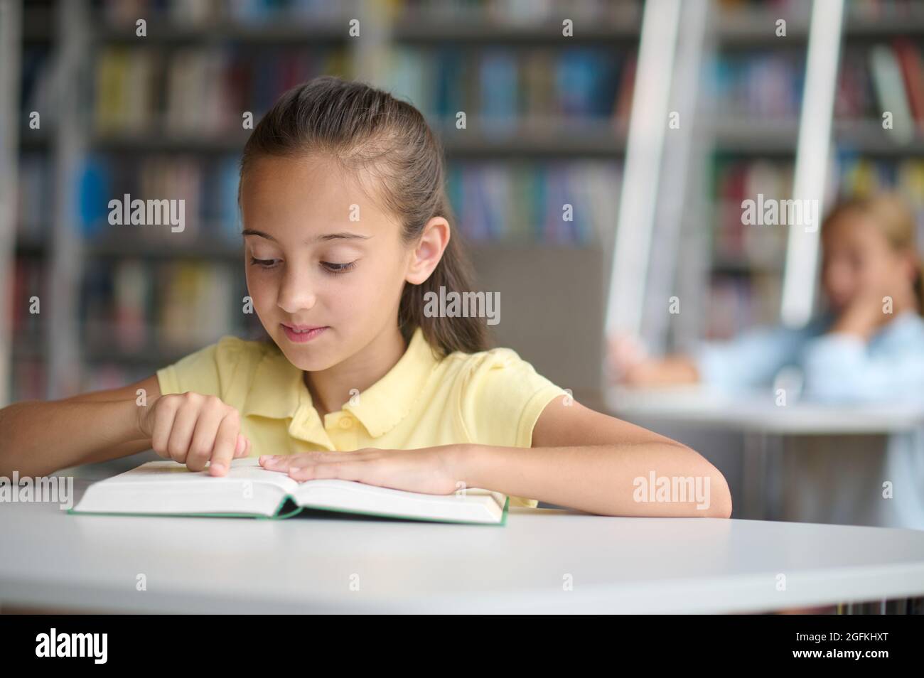 Un adorable élève se fait lire un livre au bureau de la bibliothèque Banque D'Images