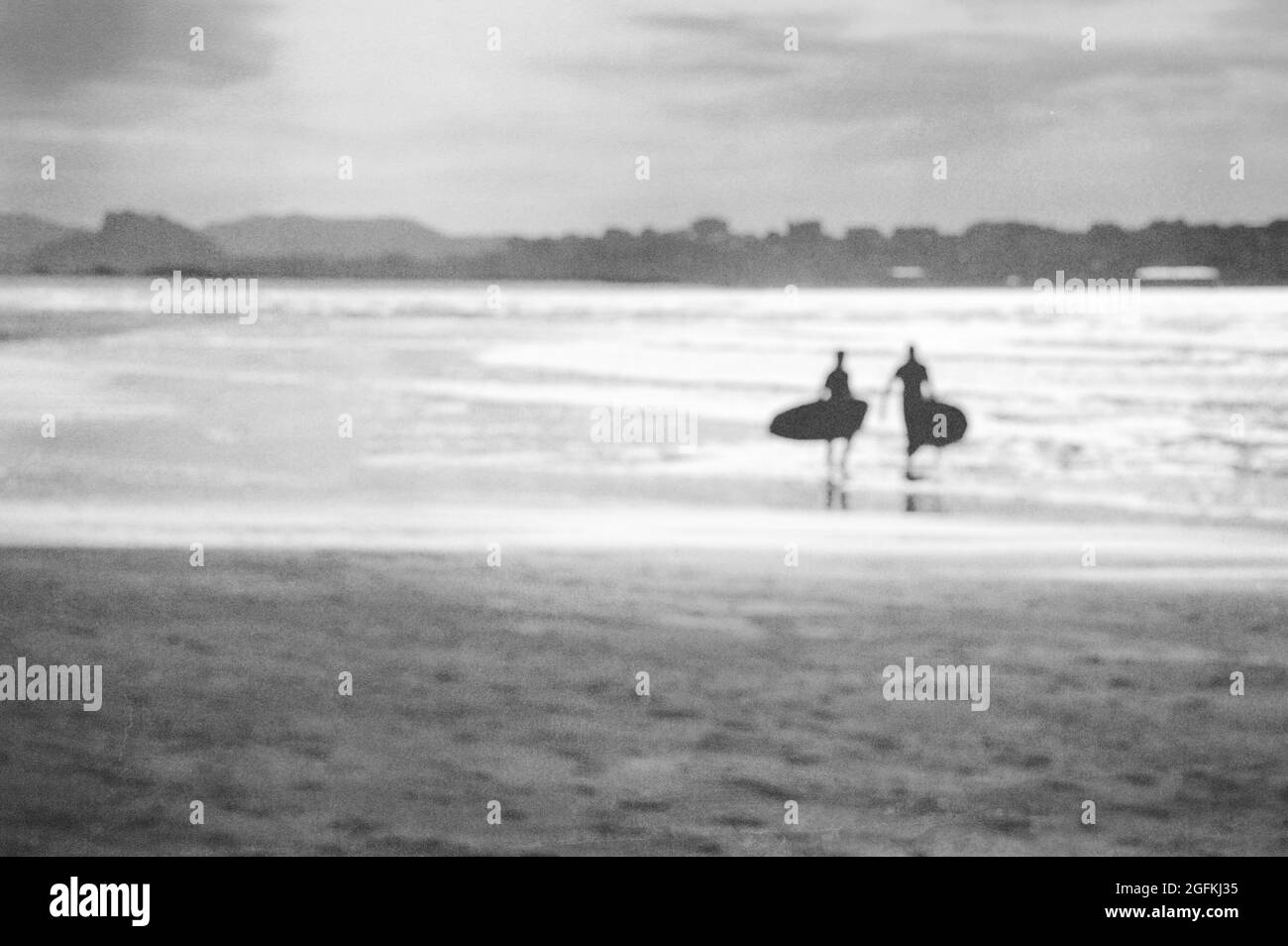 Silhouette de surfeurs transportant leur planche de surf dans la mer, avec un filtre vintage, montage flou Banque D'Images