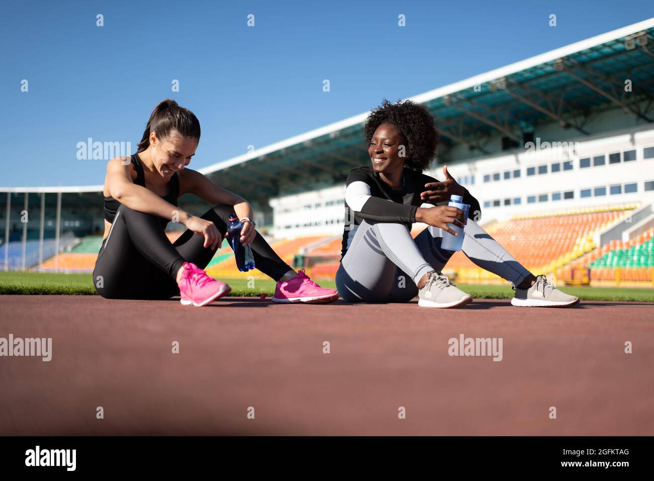 Black sportswoman en train de raconter une blague à sa petite amie tout en étant assis sur la bonne voie pendant la pause Banque D'Images